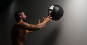 Male Athlete Crouched Doing Wall Balls Exercises At The Gym