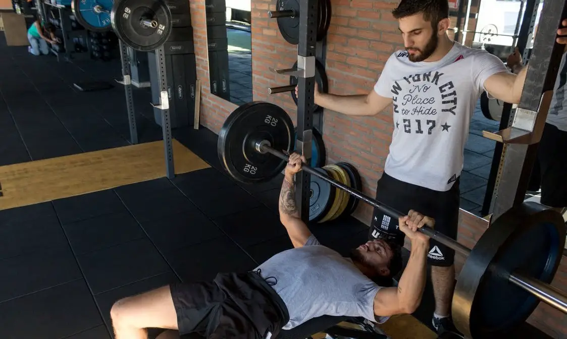 Person doing a bench press rep with a spotter